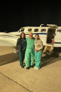 A photo of three people in surgical scrubs standing on the tarmac next to a small plane