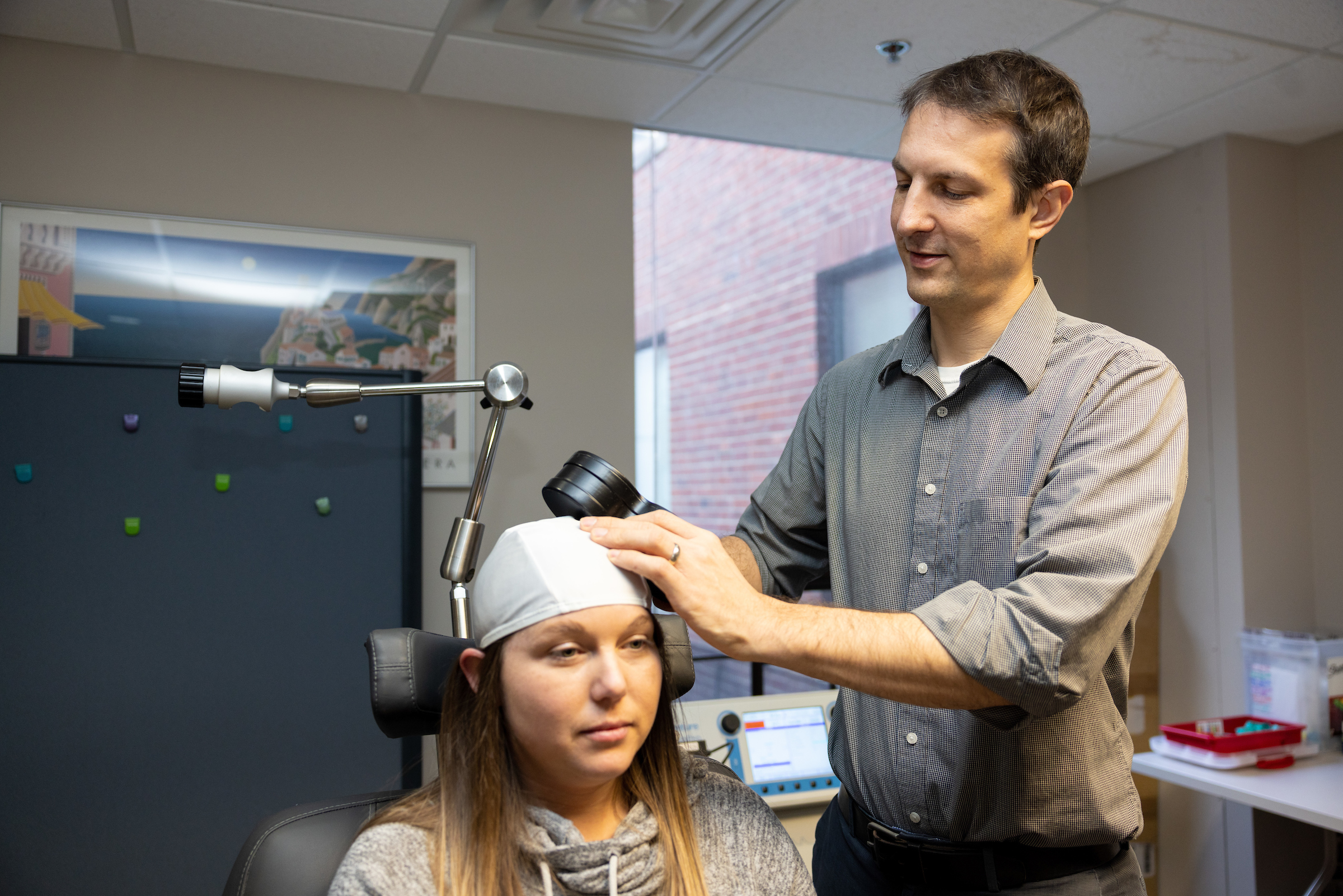 Aaron Boes applies TMS device, which looks like a white cloth cap, to a patient's head.