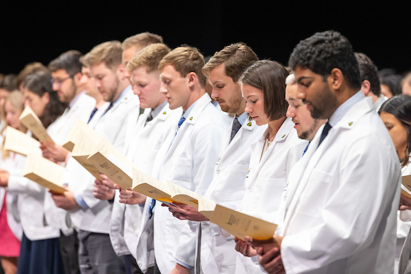 Students in white coats reading the Hippocratic Oath for the first time