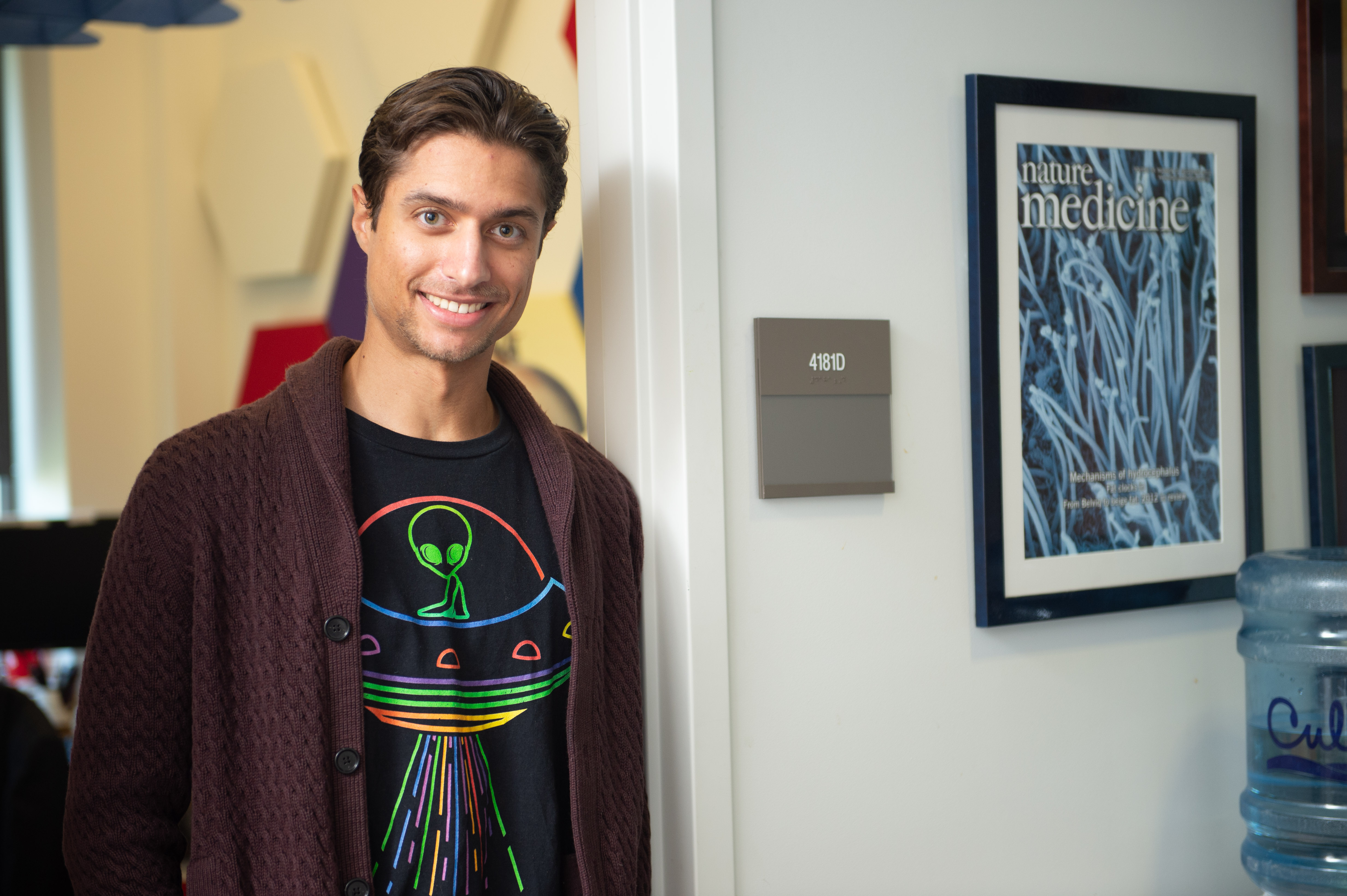 Calvin Carter standing in the doorway of his office. He is wearing a cardigan over a t-shirt with a colorful design of an alien in a flying saucer.