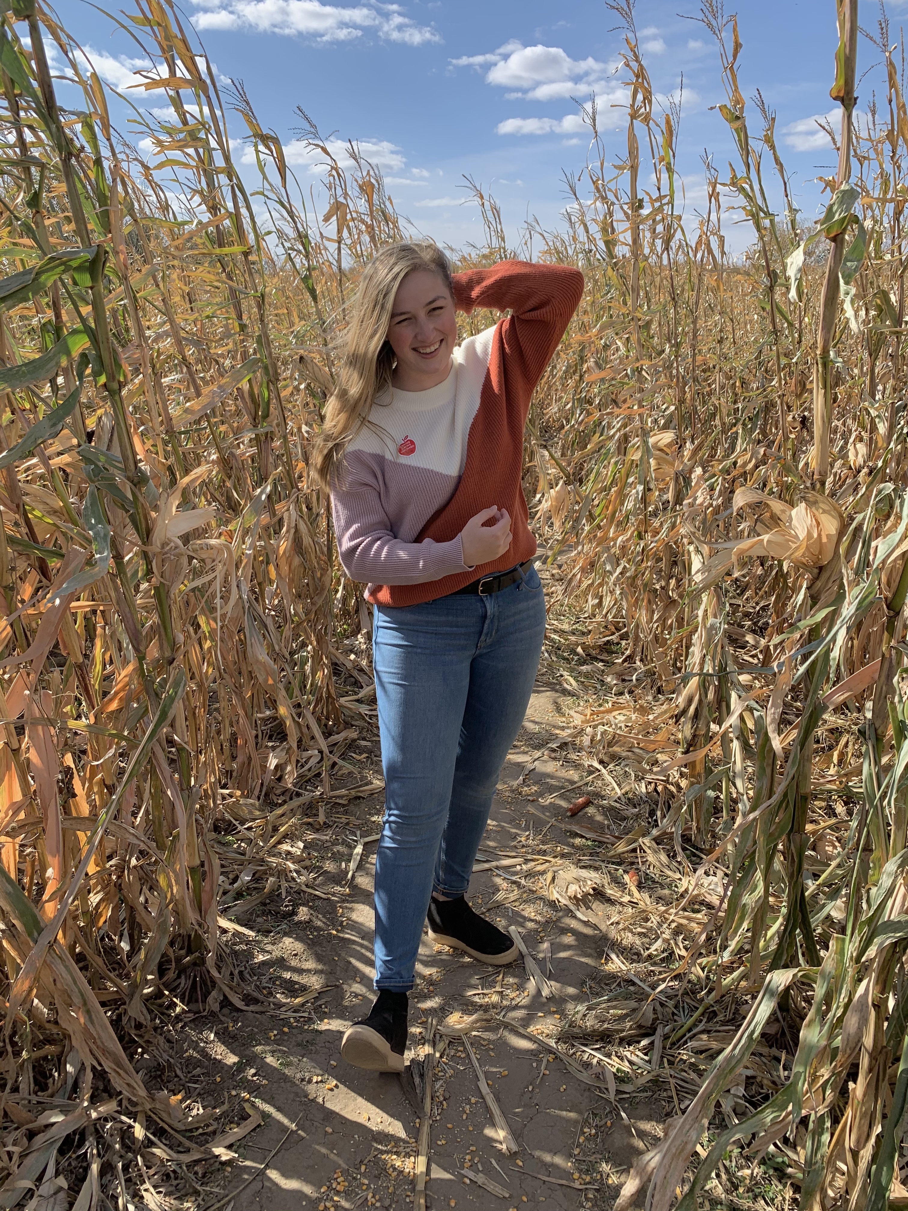 Hailey Zillig stands smiling in a corn field on a sunny autumn day