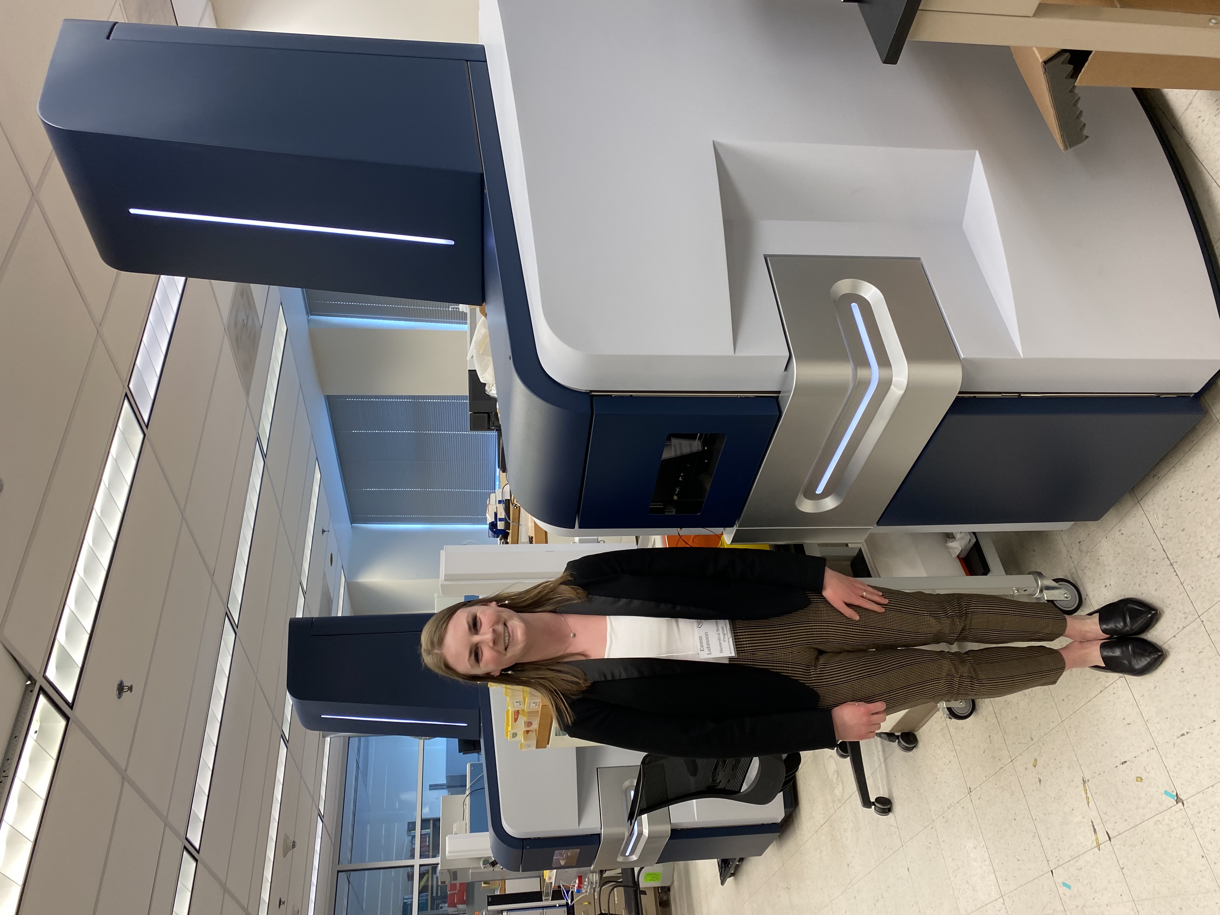 Emma Luhmann stands next to the mass spectrometer in the lab where she works.