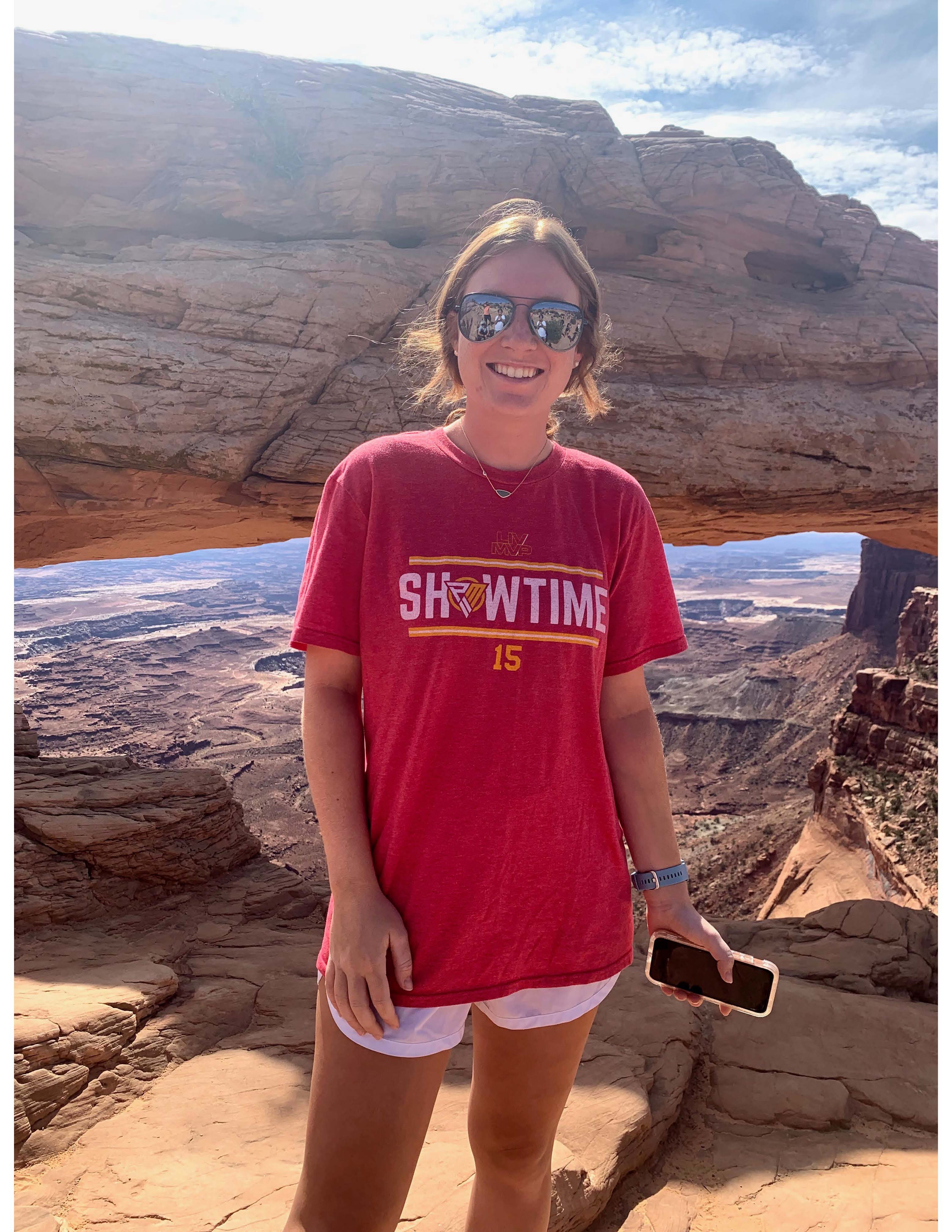 Lauren Bays stands in front of a desert canyon. She is dressed for hiking and wearing sunglasses.