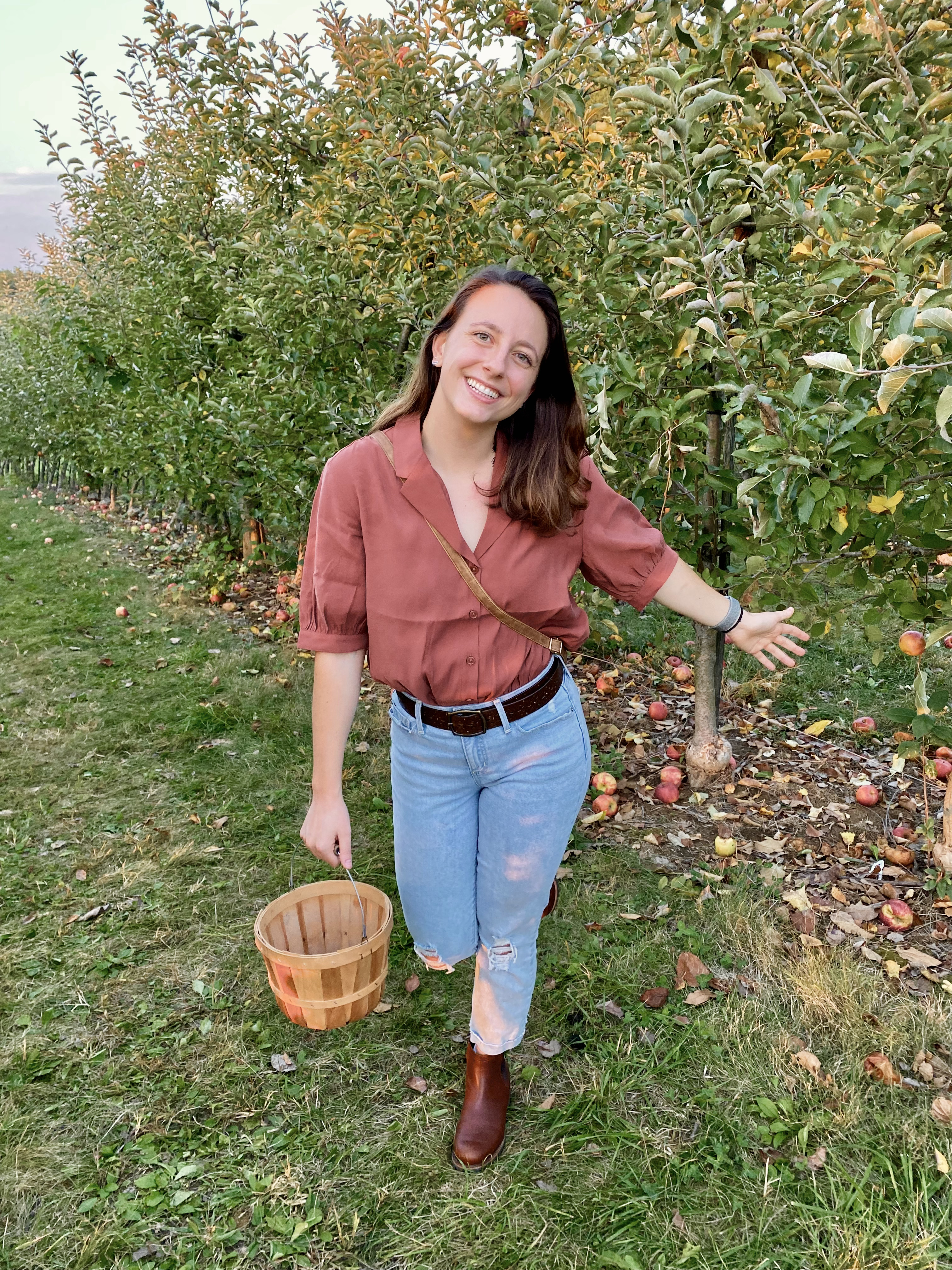 Alex Lewis smiles in an apple orchard, holding a straw bucket.