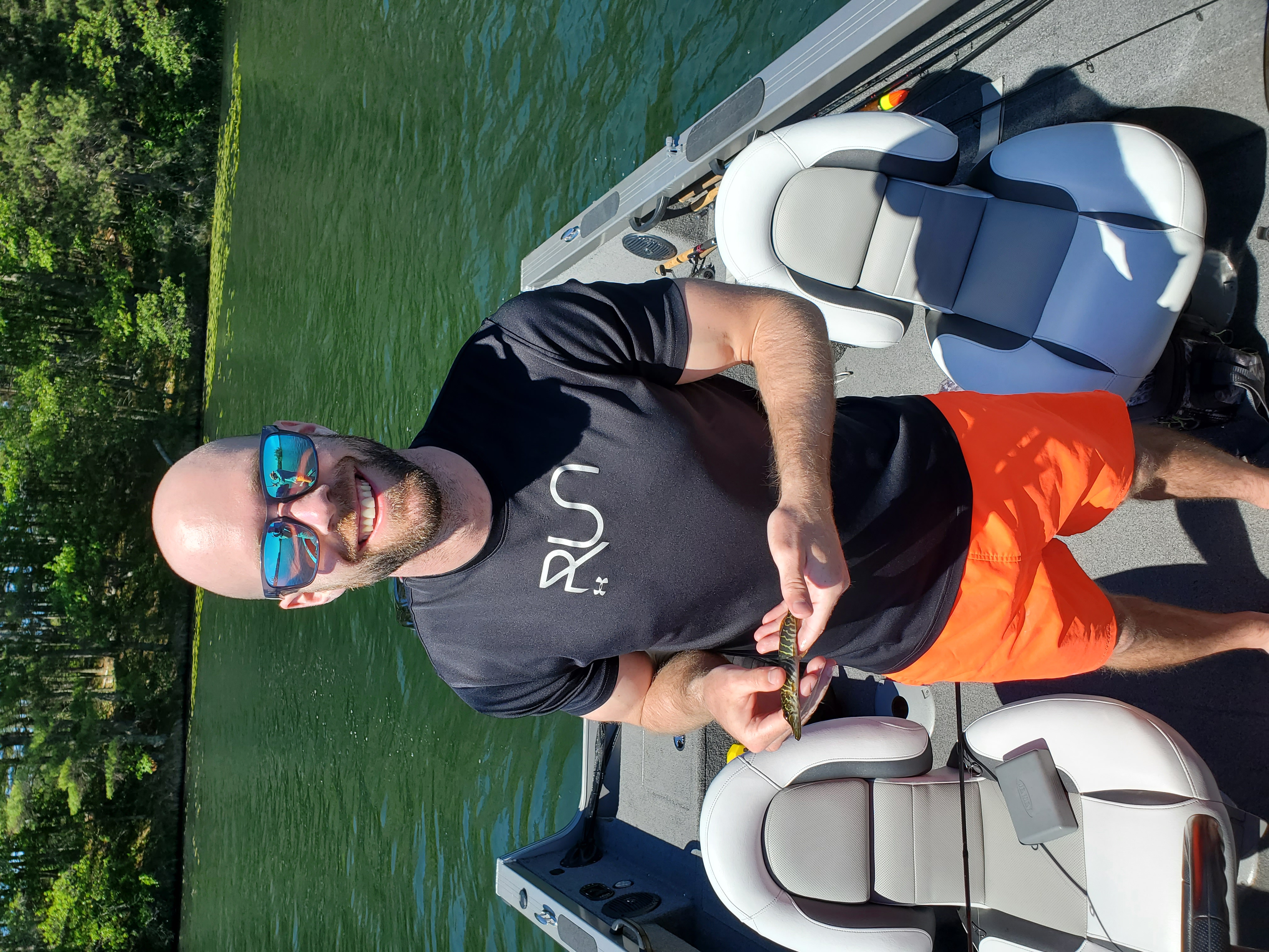 Christopher Ball stands in a boat holding a small fish and smiling