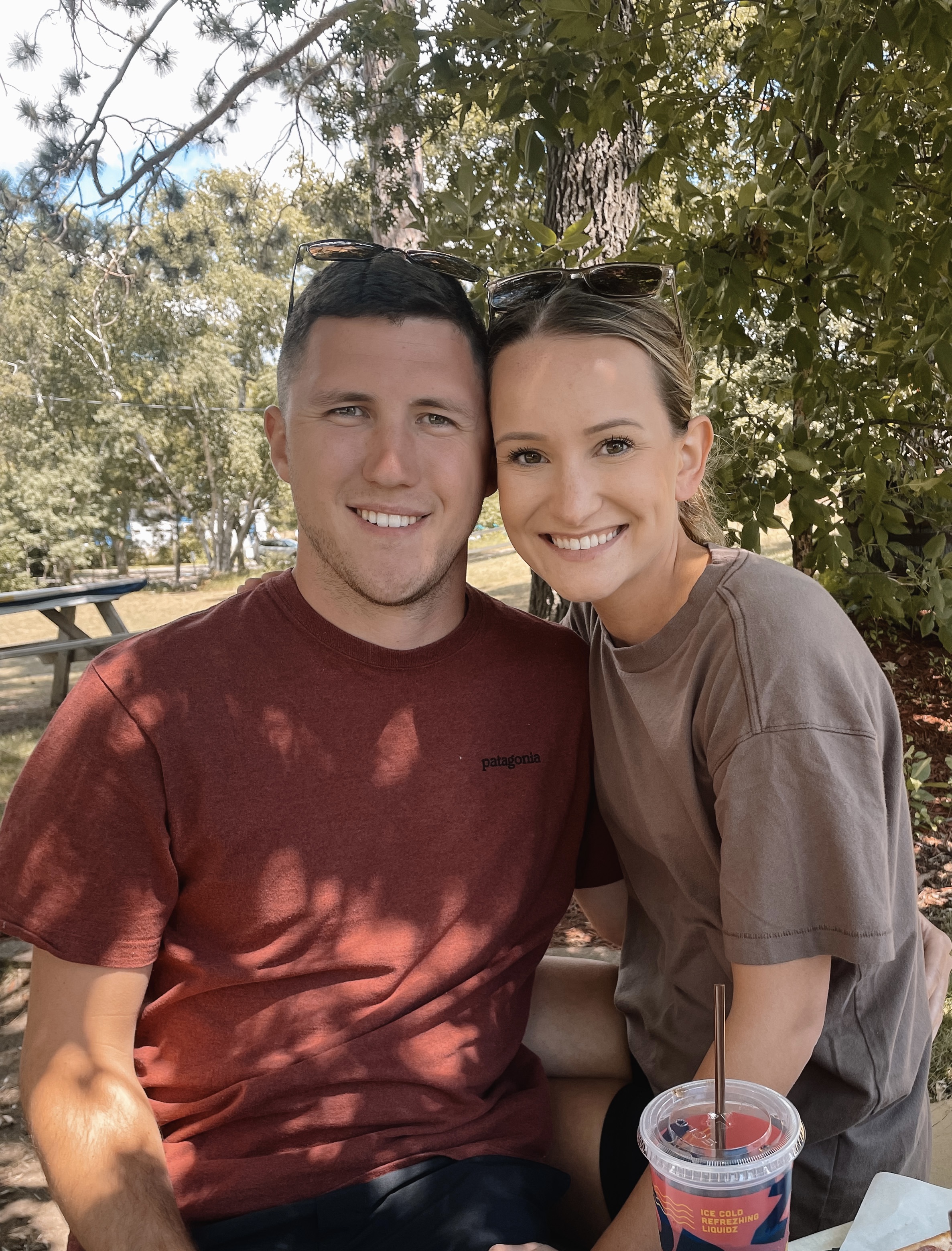Jacob Norton and his wife sit outdoors in a park, smiling at the camera.