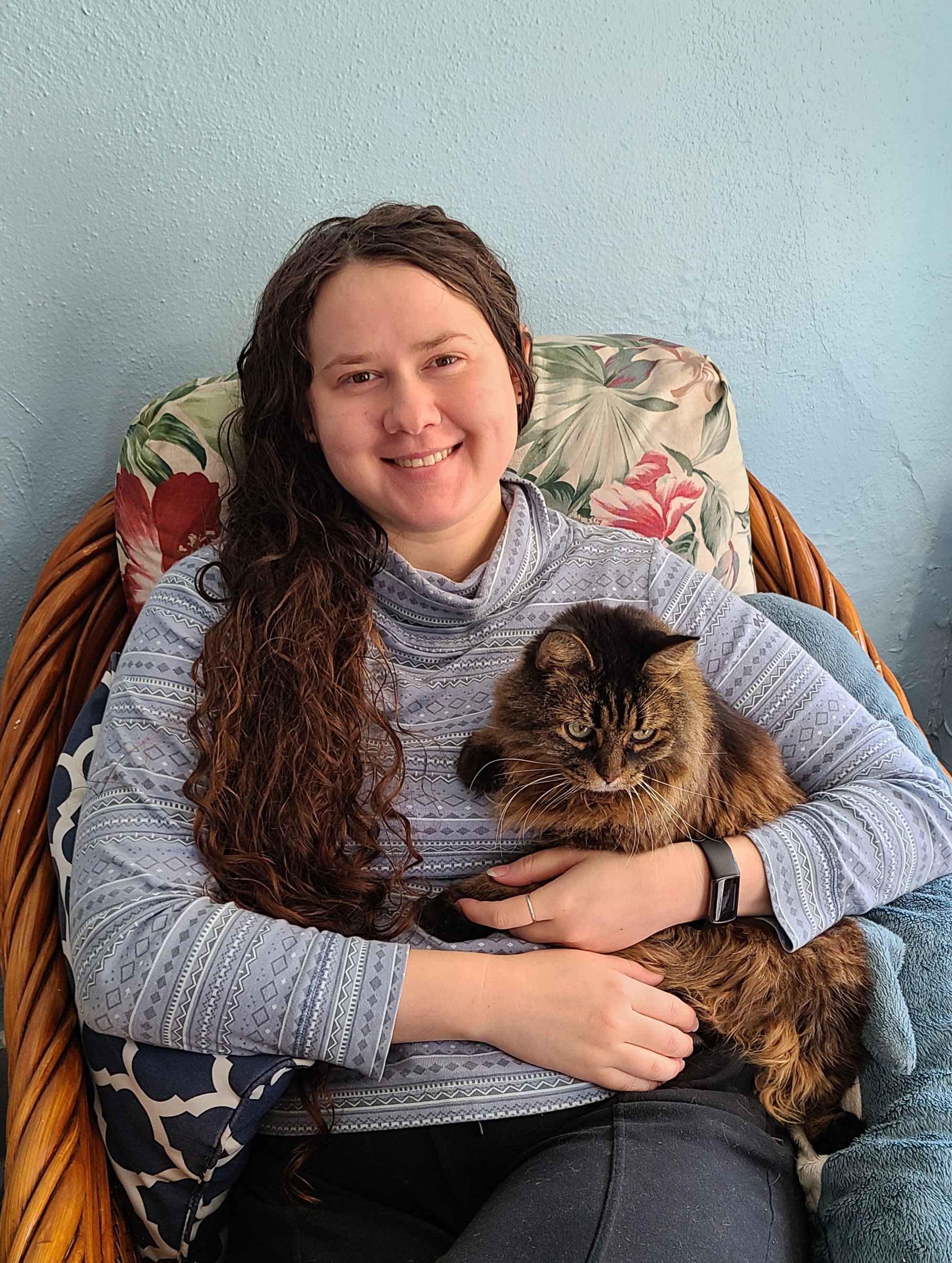 Sofiya Pisarenka sits in a wicker chair, smiling and holding a long-haired cat