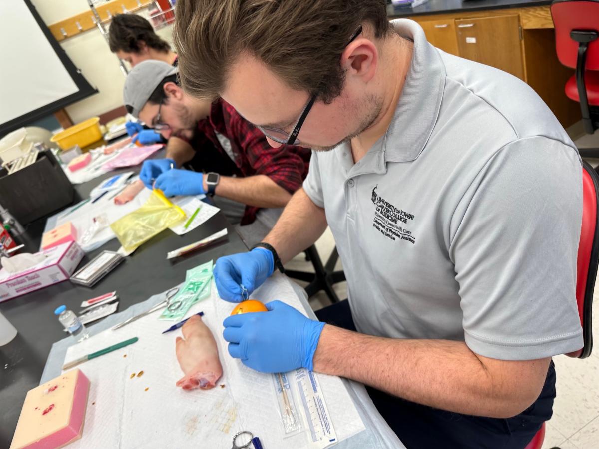 Cole Kitzman practices suturing skills on a pig's foot and an orange.