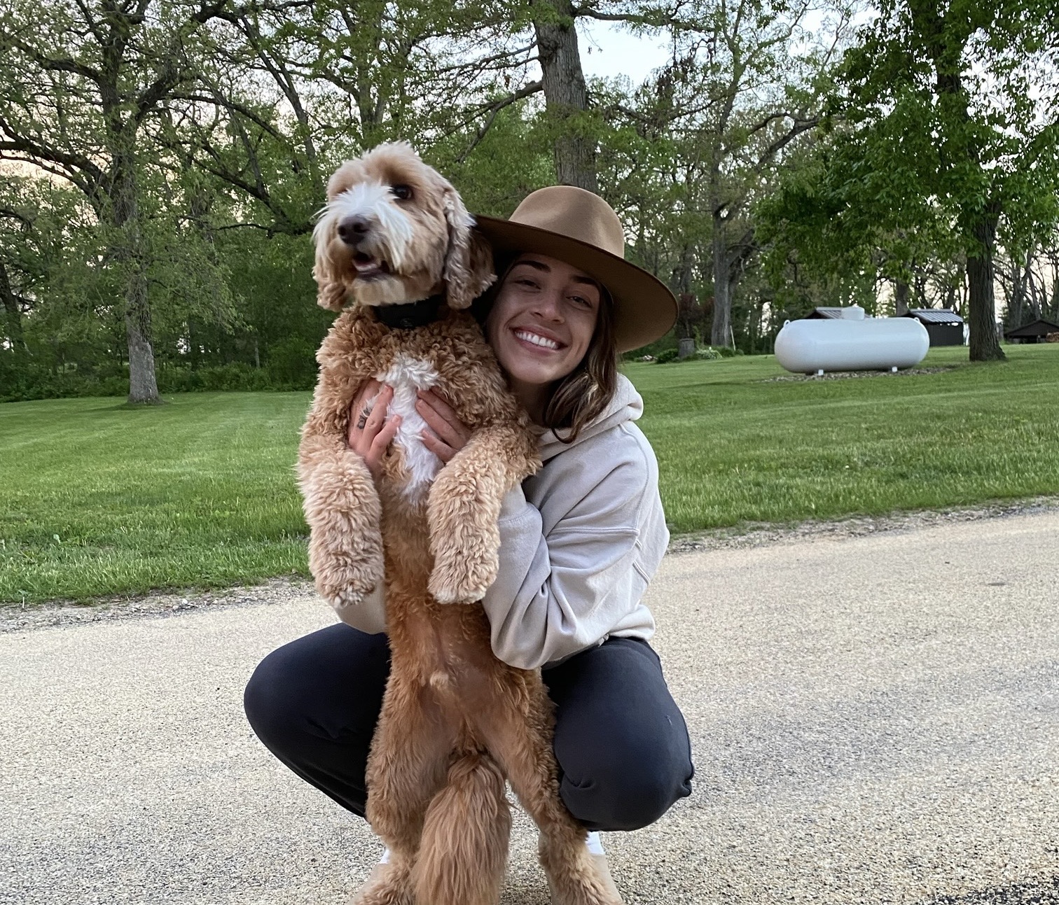 Dani Chamberlain poses outside with a fluffy dog standing on its hind legs.