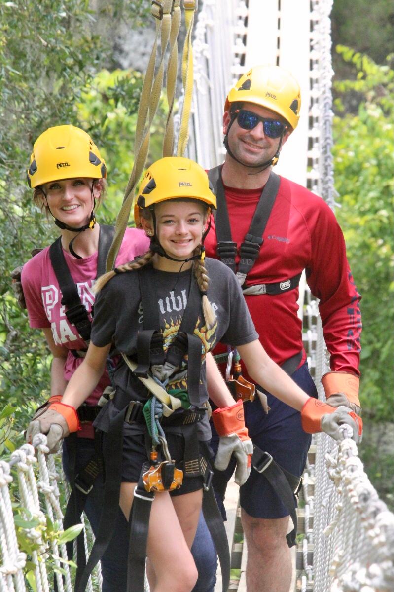 John Hanshew and his family stand together in helmets and harnesses on a high rope bridge.
