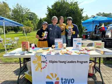 Palma stands at an outdoor booth with three other people who are all smiling. The booth says, "Tayo Filipino Young Leaders Program."