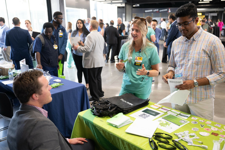 A trainee physician speaks to an exhibitor seated at a table